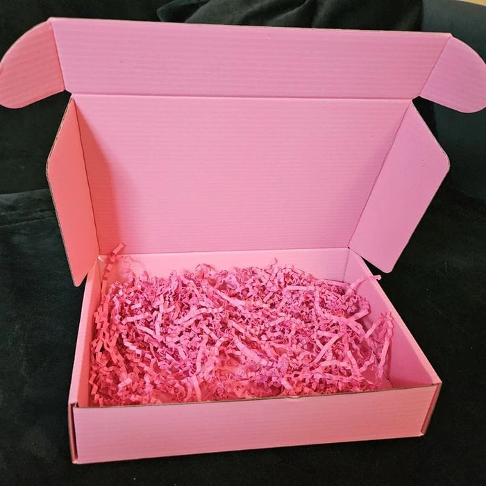 A pink shipping box open on its shredded-paper filler